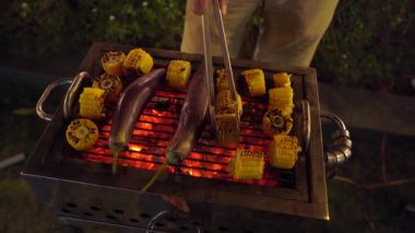 Gece barbekü. Adam ızgarada sebze pişiriyor.