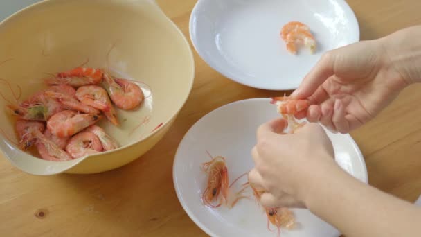 Une femme épluche des crevettes sur une table en bois — Video