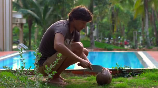 Ung man i tropikerna öppnar en gammal kokosnöt med en stor kniv — Stockvideo