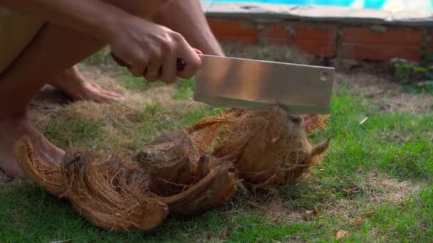 Młody człowiek w tropikach otwiera starego kokosa wielkim nożem — Wideo stockowe