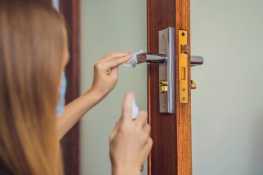 Kadın eli kapı koluna dezenfektan sürüyor. Covid-19 Coronavirus önleme ilacı ile kapı kolunu temizliyorum. Alkol sıkarak kapı kolunu dezenfekte etmek.