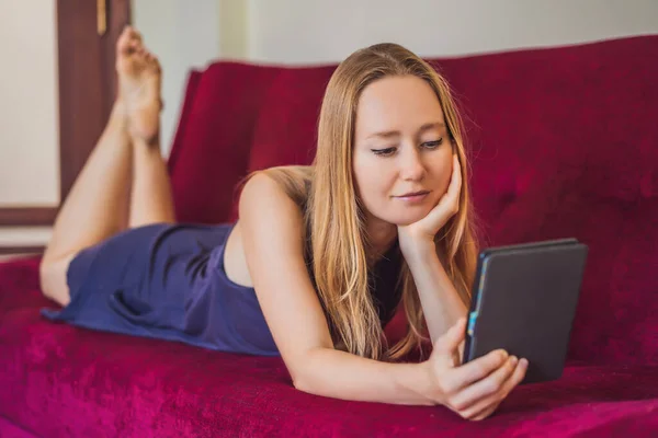 Młoda kobieta czyta e-booki w domu na kanapie — Zdjęcie stockowe