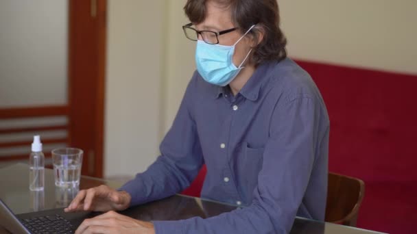 얼굴에 마스크를 쓰고 있는 젊은 남자가 코로나 바이러스가 혼자 있는 동안 집에서 일한다 — 비디오