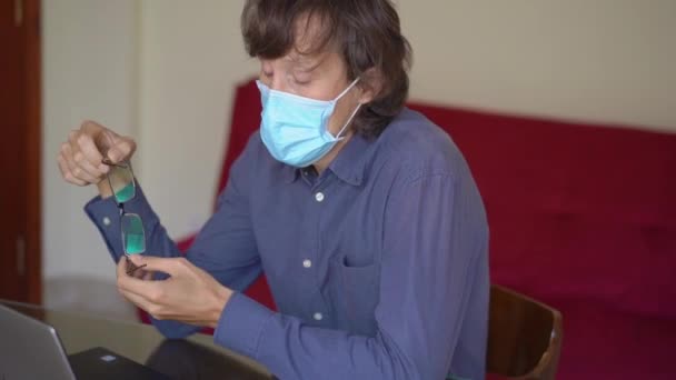 Een jongeman met een gezichtsmasker werkt vanuit huis tijdens de zelfisolatie van het coronavirus. Hij is het beu om thuis te blijven en bezorgd te zijn over de toekomst. Langzame schot — Stockvideo