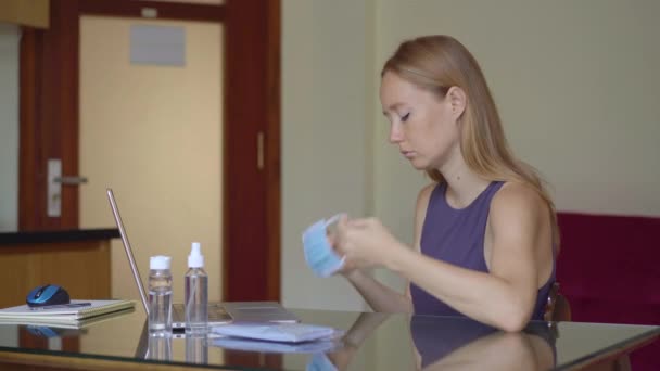 若い女性は、医療用フェイスマスクを着用し、コロナウイルスの自己分離中に自宅から作品 — ストック動画