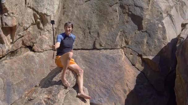 Un joven sentado en el borde de un acantilado haciendo un video selfie — Vídeos de Stock