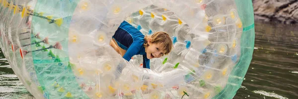 Söt liten pojke, spelar i Zorb en rullande plastcylinder ring med ett hål i mitten på sjön BANNER, LONG FORMAT — Stockfoto