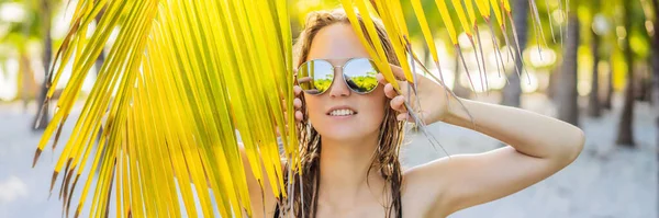 young beautiful woman in swimsuit on tropical beach, summer vacation, palm tree leaf, tanned skin, sand, smiling, happy. Happy traveller woman BANNER, LONG FORMAT