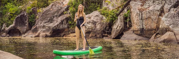 SUP Stand up κουπί του σκάφους γυναίκα κουπί επιβίβασης στη λίμνη στέκεται ευτυχισμένη στο paddleboard σε μπλε νερό. Action Shot of Young Woman on Paddle Board BANNER, μακρινή φόρμα — Φωτογραφία Αρχείου