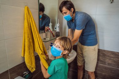 Baba oğluna ellerini doğru dürüst yıkamayı öğretiyor. Koronovirüs yüzünden maskeli baba ve oğul. Salgın hastalık. Evde kal. Ellerini yıka.