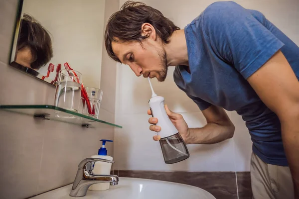 A man uses an oral irrigator in his bathroom — Stock Photo, Image