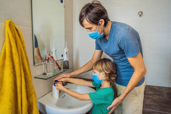 Dad teaches his son to wash his hands properly. Dad and son in medical masks because of coronovirus. Epidemic. Stay home. Wash your hands