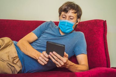 E-kitap ve online eğitim. Bir adam evde karantinaya alınmış bir kitap okuyor. Tıbbi maskeli bir adam evde tek başına kaldı.