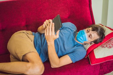 E-kitap ve online eğitim. Bir adam evde karantinaya alınmış bir kitap okuyor. Tıbbi maskeli bir adam evde tek başına kaldı.