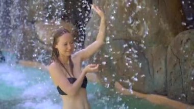 Sıcak pınarları, şelaleleri ve sıcak maden suyu olan yüzme havuzları olan tropikal bir tatil köyünde genç bir kadın. Yavaş çekim.