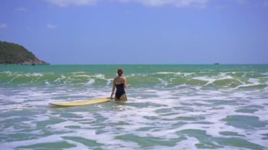 Genç bir kadının yavaş çekimi güzel bir denizde sörf yapıyor.