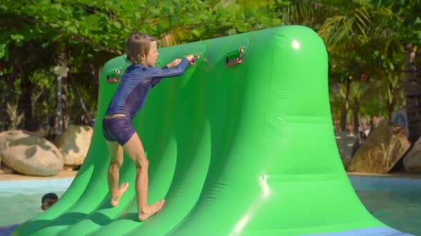 Niño pequeño en una carrera de obstáculos inflable en un parque acuático. Concepto de verano — Vídeos de Stock