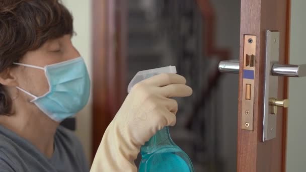 Un joven con una máscara médica desinfecta la manija de la puerta durante el autoaislamiento. Concepto de distanciamiento social — Vídeo de stock