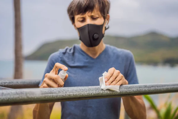 Az ember fertőtleníti a vízszintes rudat sport előtt. Egy férfi orvosi maszkban sportolt a koronavírus járvány alatt. — Stock Fotó