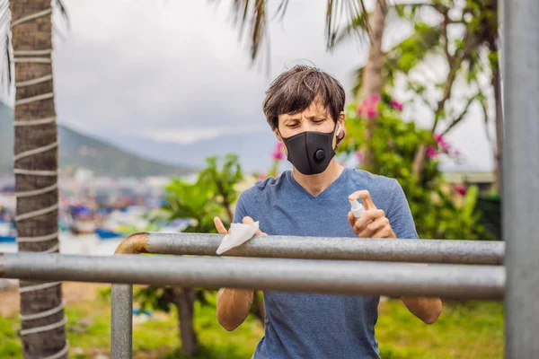 Mann desinfiziert Querstange vor Sport. Ein Mann mit medizinischer Maske treibt während der Coronavirus-Epidemie Sport — Stockfoto