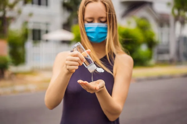 Kobieta w małym miasteczku w masce medycznej używa środka dezynfekującego z powodu epidemii koronowirusa. — Zdjęcie stockowe