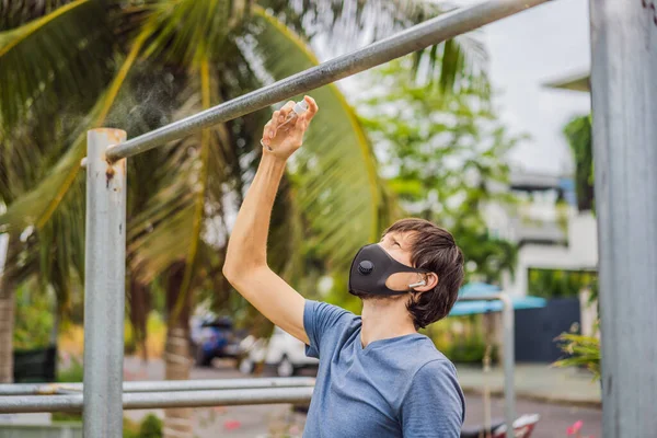 Mann desinfiziert Querstange vor Sport. Ein Mann mit medizinischer Maske treibt während der Coronavirus-Epidemie Sport — Stockfoto