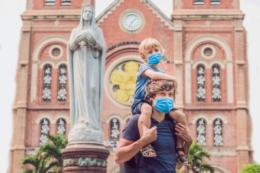 Arka planda tıbbi maskeli baba ve oğul Notre dame de Saigon Katedrali, 1883 'te Ho Chi Minh şehrinde inşa edildi, Vietnam Turistleri 2019-ncov virüsünden korkuyorlar. Tıbbi maskeli turistler
