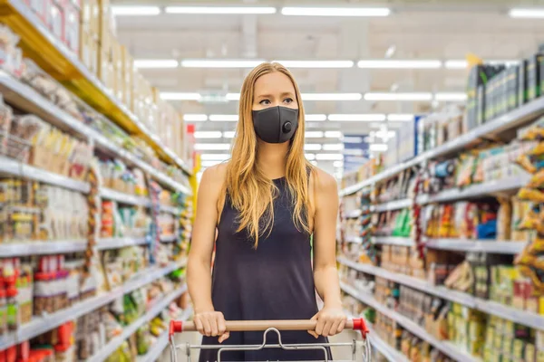Alarmed female wears medical mask against coronavirus while grocery shopping in supermarket or store- health, safety and pandemic concept - young woman wearing protective mask and stockpiling food