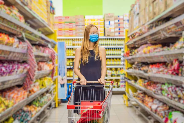 경계하고 있는 여성은 코로나 바이러스에 대항하여 의료용 마스크를 쓰고 슈퍼마켓이나 상점에서 식품을 사는 동안 건강, 안전, 유행병처럼 번지는 개념 - 보호용 마스크를 쓰고 식품을 비축하는 젊은 여성 — 스톡 사진