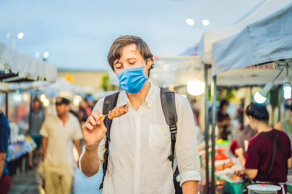 Young man tourist in medical mask on Walking street Asian food market Tourists fear the 2019-ncov virus. Medical masked tourists — Stock Photo, Image