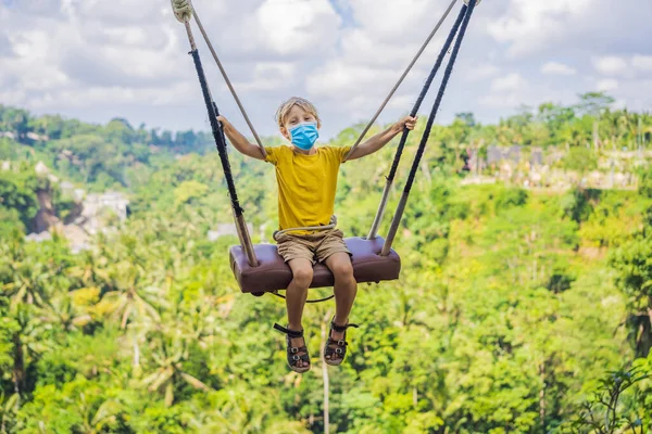 身穿医疗面罩的小男孩在印度尼西亚巴厘岛的热带雨林里荡秋千。在热带地区荡秋千摇摆-巴厘的趋势。带着孩子旅行的概念。孩子们该怎么办？儿童 — 图库照片