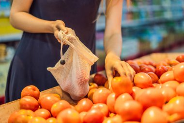 Bir kadın süpermarkette plastik torba kullanmadan domates seçer. Sebze almak için tekrar kullanılabilir çanta. Sıfır atık