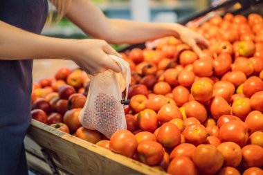 Bir kadın süpermarkette plastik torba kullanmadan domates seçer. Sebze almak için tekrar kullanılabilir çanta. Sıfır atık
