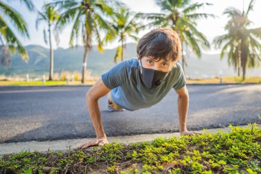 Coronavirus karantinası sırasında parkta egzersiz yapan maskeli genç bir adam.