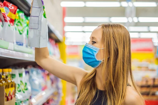 Alarmed female wears medical mask against coronavirus while grocery shopping in supermarket or store- health, safety and pandemic concept - young woman wearing protective mask and stockpiling food