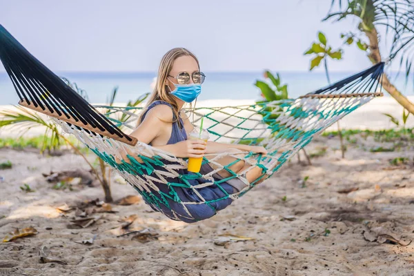 Mujer joven con máscara médica en la playa en una hamaca con una bebida Los turistas temen el virus 2019-ncov. Turistas médicos enmascarados —  Fotos de Stock