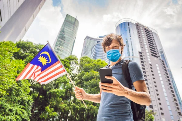Travel and technology. Young man in medical mask tourist with the flag of Malaysia is looking at a city map in a smartphone for navigation Tourists fear the 2019-ncov virus. Medical masked tourists