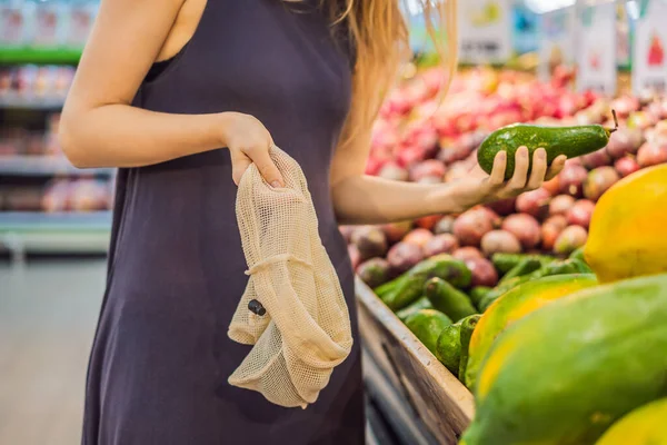 La mujer elige aguacate en un supermercado sin usar una bolsa de plástico. Bolsa reutilizable para comprar verduras. Concepto de cero residuos — Foto de Stock