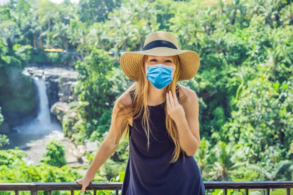 Woman in medical mask traveler on a waterfall background. Ecotourism concept Tourists fear the 2019-ncov virus. Medical masked tourists — Stock Photo, Image