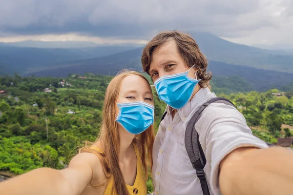 Homme et femme en masque médical faisant du selfie sur fond de volcan Batur et vue sur la montagne Agung le matin depuis Kintamani, Bali, Indonésie Les touristes craignent le virus 2019-ncov. Touristes masqués médicaux — Photo