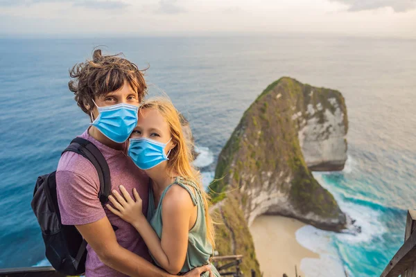 Family vacation lifestyle. Happy couple - man and woman in medical mask stand at viewpoint. Look at beautiful beach under high cliff. Travel destination in Bali. Popular place to visit on Nusa Penida — Stock Photo, Image
