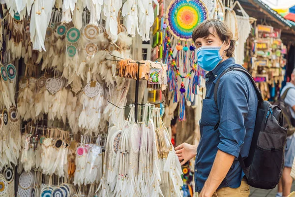 Man in medical mask at a market in Ubud, Bali. Typical souvenir shop selling souvenirs and handicrafts of Bali at the famous Ubud Market, Indonesia. Balinese market. Souvenirs of wood and crafts of — Stock Photo, Image