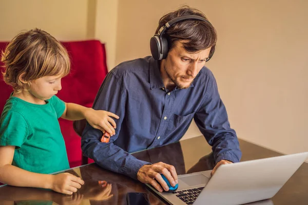 Man is trying to work from home because of the coronovirus epidemic, but his son is stopping him. Self-isolation at home. Children at home schooling. Parents at remote work. Quarantine, self-isolation