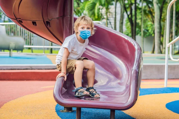 Engraçado bebê feliz bonito em máscara médica jogando no parque infantil. A emoção da felicidade, diversão, alegria Os turistas temem o vírus 2019-ncov. turistas mascarados médicos — Fotografia de Stock