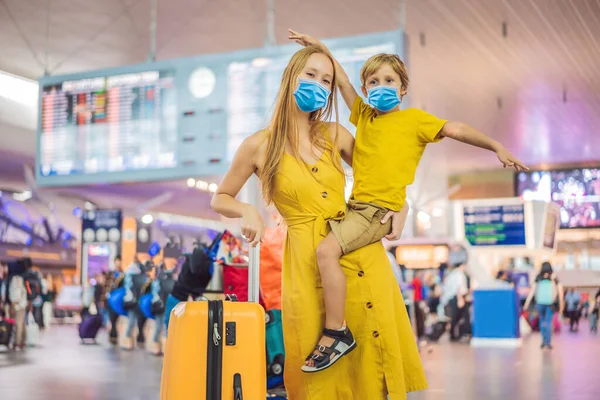 Family at airport before flight. Mother and son in medical mask waiting to board at departure gate of modern international terminal. Traveling and flying with children. Mom with kid boarding airplane