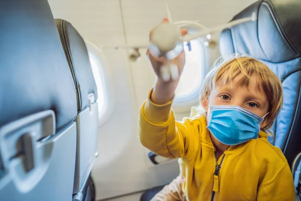 Menino de máscara médica brinca com avião de brinquedo no avião comercial voando em férias Turistas temem o vírus 2019-ncov. turistas mascarados médicos — Fotografia de Stock