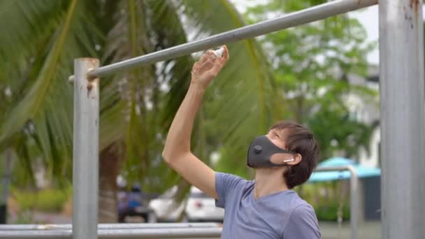 A young man disinfects pull-up bar on a street. Then he starts doing exercises. Physical exercises during the quarantine — Stock Video