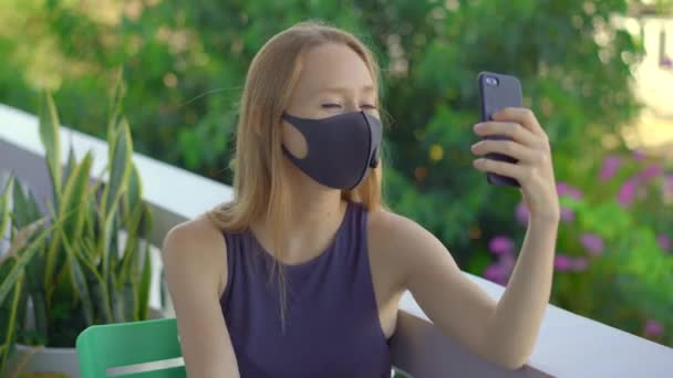 Mujer joven, con una máscara facial de tejido, habla en un teléfono inteligente. Las máscaras a la moda. Concepto de distanciamiento social — Vídeos de Stock