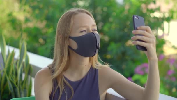 Giovane donna, indossando una maschera di tessuto, parla su uno smartphone. Maschere facciali alla moda. Concetto di distanza sociale — Video Stock