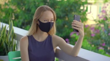 Doku maskesi takan genç bir kadın akıllı telefondan konuşuyor. Modaya uygun yüz maskeleri. Sosyal uzaklık kavramı